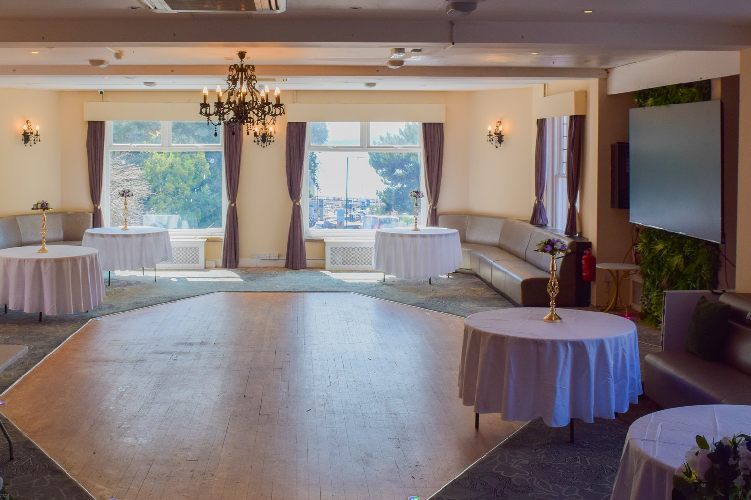 The function room at Ashbury Lounge in daylight, set with round tables, a dance floor and floor-to-ceiling windows