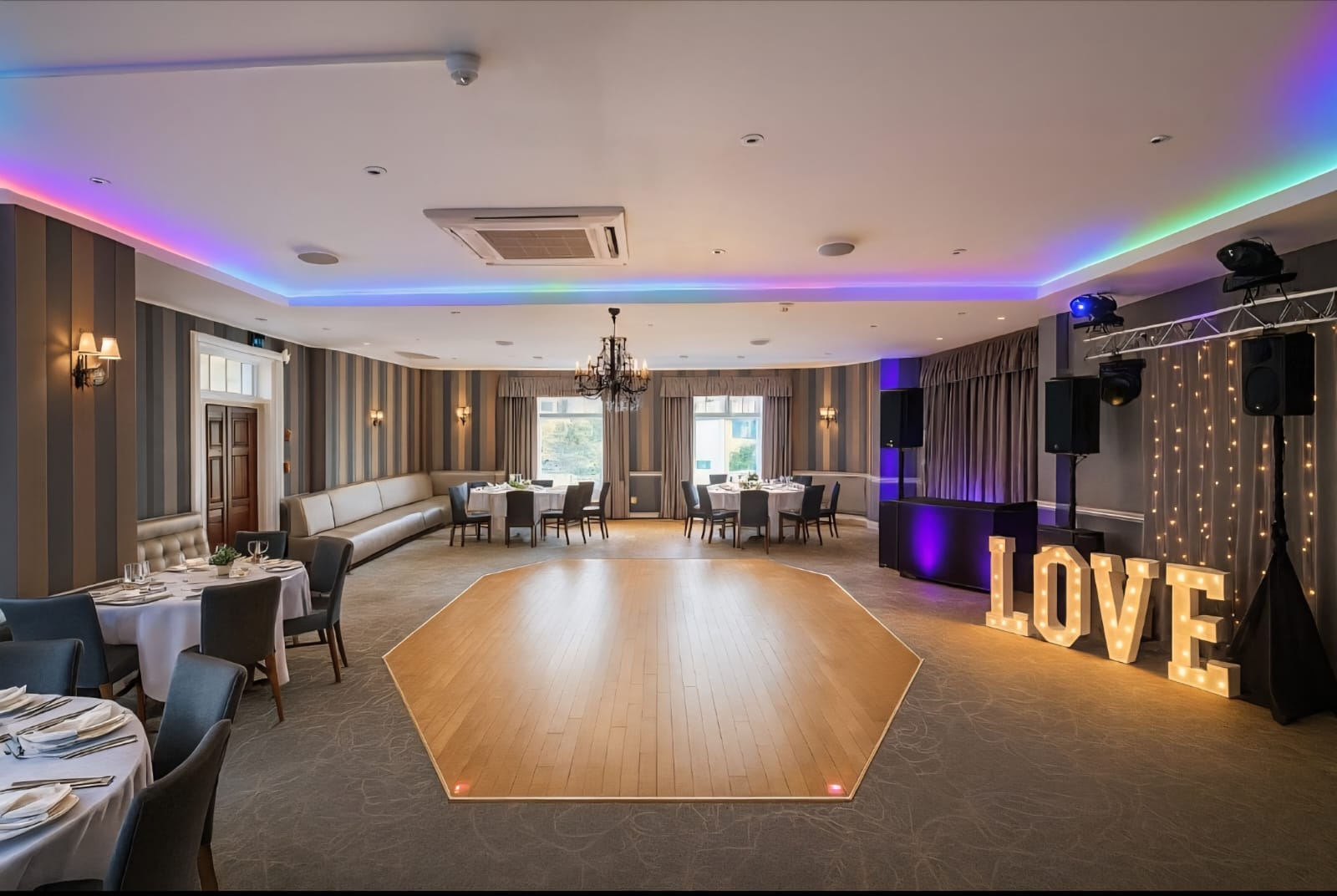 The function room at Ashbury Lounge with a wooden dance floor in the middle, DJ speakers and lit LOVE letters at one end, and round tables laid at the edges