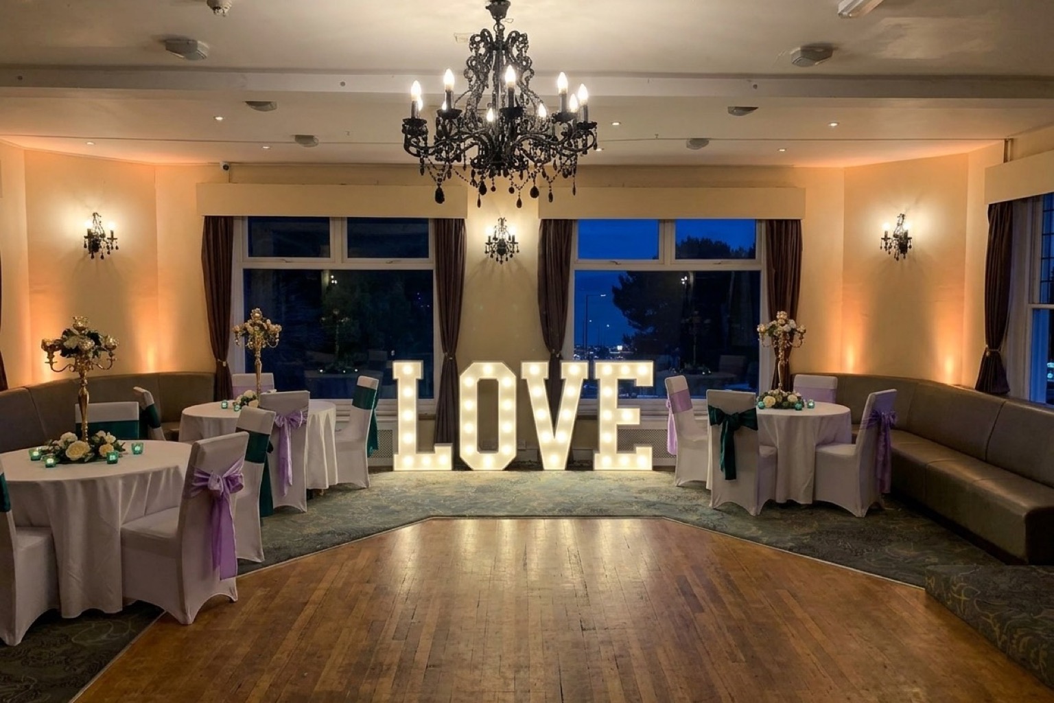 The function room at Ashbury Lounge in the evening, set with round tables either side of the dance floor and lit LOVE letters